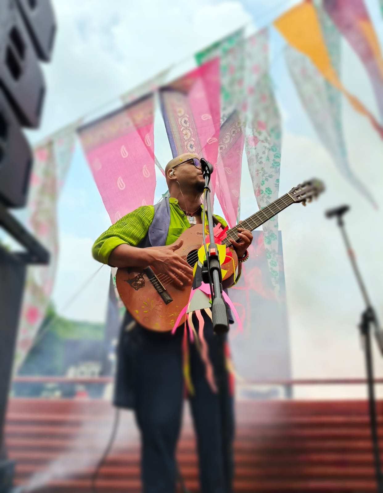 Saji Oorali performing on an outdoor stage hung with printed cloth bunting.